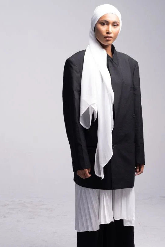 A woman wearing a white pashmina headscarf over a black outfit against a grey background.