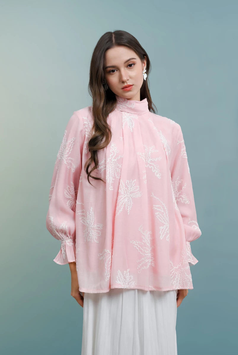 Woman wearing a pink blouse with white floral patterns by Kasa Heritage on a gradient background