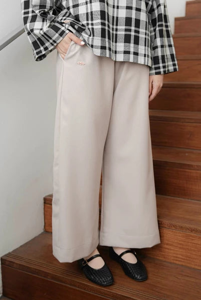 Person wearing a black and white checkered shirt and beige culotte pants by Mistyvori standing on wooden stairs.
Seorang wanita mengenakan kemeja kotak-kotak hitam-putih dan celana kulot berwarna beige dari Mistyvori berdiri di tangga kayu.
