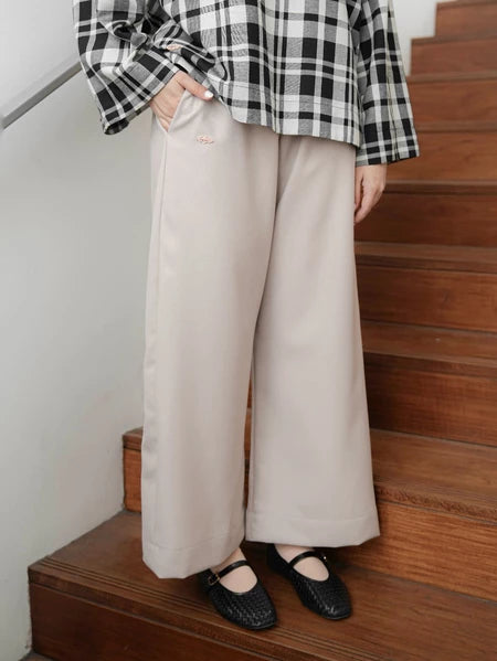 Person wearing a black and white checkered shirt and beige culotte pants by Mistyvori standing on wooden stairs.
Seorang wanita mengenakan kemeja kotak-kotak hitam-putih dan celana kulot berwarna beige dari Mistyvori berdiri di tangga kayu.