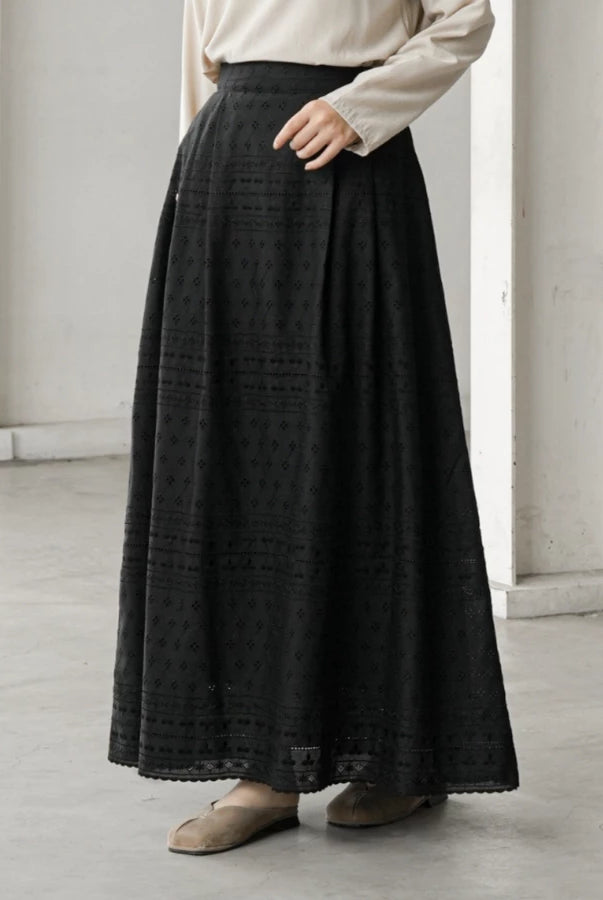 Person wearing a long black patterned skirt by Mistyvori with a white shirt in a minimalistic setting