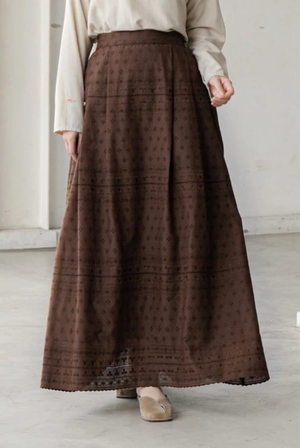 Person wearing a long brown patterned skirt by Mistyvori with a white top in a minimalistic setting