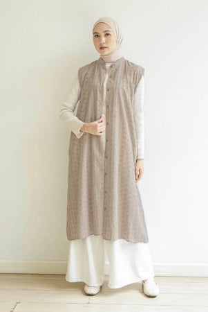 Woman wearing a long, patterned taupe-colored vest by Mistyvori over a white outfit against a plain background