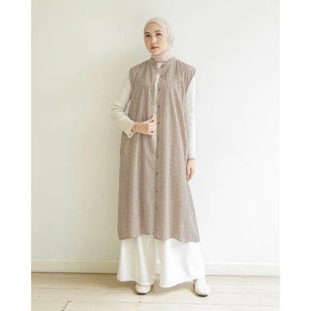 Woman wearing a long, patterned taupe-colored vest by Mistyvori over a white outfit against a plain background