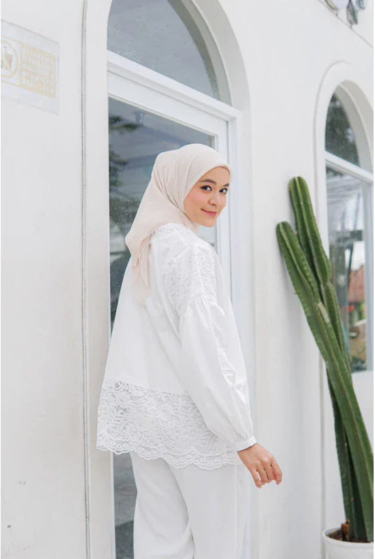 A person wearing a white balloon sleeve shirt with lace details by Casa Elana, paired with white trousers, standing next to a cactus plant.