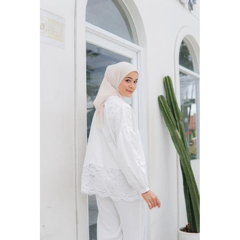 A person wearing a white balloon sleeve shirt with lace details by Casa Elana, paired with white trousers, standing next to a cactus plant.