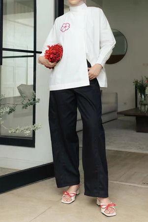 Person wearing a white shirt and black barrel pants from Haidee Orlin holding red flowers in a modern indoor setting.