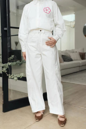 Person wearing a white shirt and white barrel pants from Haidee Orlin holding red flowers in a modern indoor setting.