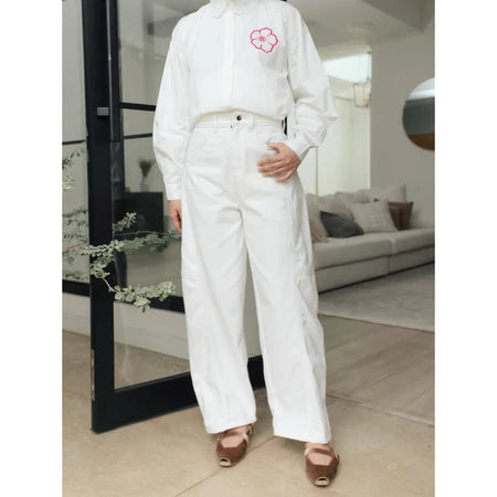 Person wearing a white shirt and white barrel pants from Haidee Orlin holding red flowers in a modern indoor setting.