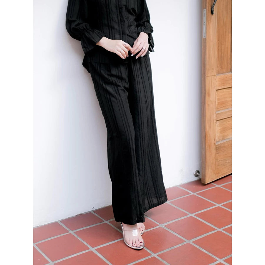 Person wearing a black pants by Renaette standing on a red-tiled floor against a white wall.