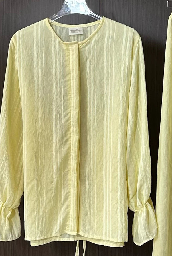 Light yellow blouse with long sleeves by Renaette on a hanger against a dark background