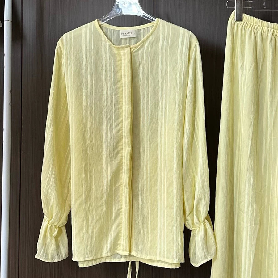Light yellow blouse with long sleeves by Renaette on a hanger against a dark background