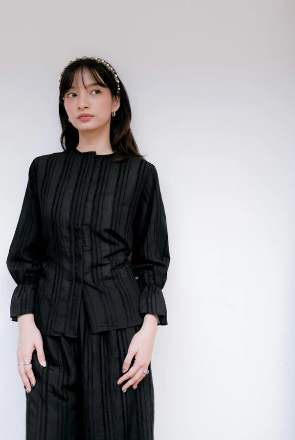 Woman wearing a black pleated blouse by Renaette against a white background