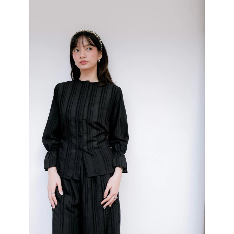 Woman wearing a black pleated blouse by Renaette against a white background