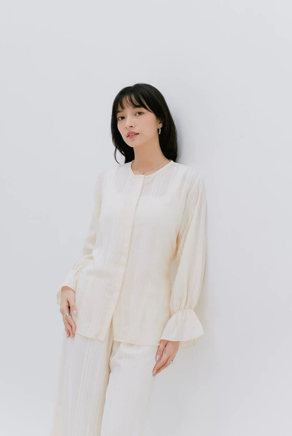 Woman wearing a cream blouse by Renaette against a light gray background