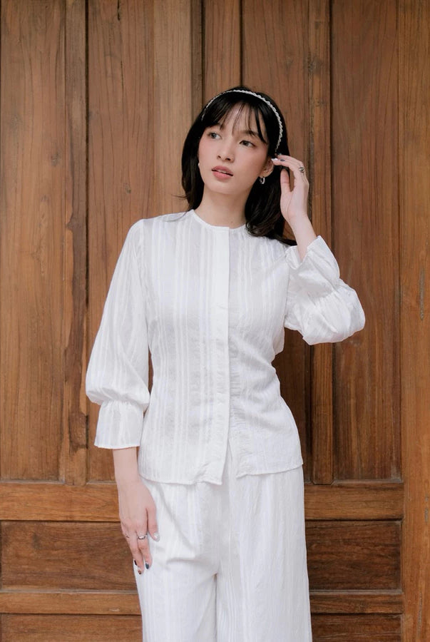 Woman in a white pleated blouse by Renaette standing in front of a wooden door