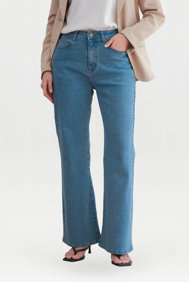 A model wearing a pair of medium-wash blue flare denim pants, styled with a beige blazer, white top, and black sandals against a plain white studio background.
Seorang model mengenakan celana denim flare berwarna biru dengan warna medium-wash, dipadukan dengan blazer krem, atasan putih, dan sandal hitam, dengan latar belakang studio berwarna putih polos.