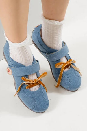 Blue flat shoes with strap and brown laces by Dianable worn with white socks on a light background