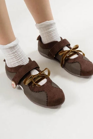 Brown flat shoes with strap bow laces by Dianable worn with white socks on a light background