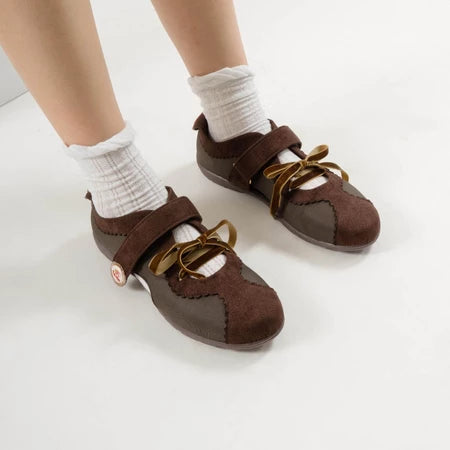 Brown flat shoes with strap bow laces by Dianable worn with white socks on a light background
