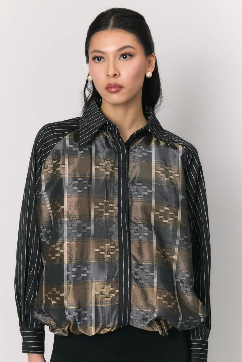 A woman modeling a sheer long-sleeve jacket by Studio Tui with a geometric plaid pattern in brown, beige, and gray, paired with black pinstriped sleeves and a black collar.