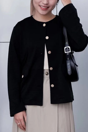 A woman wearing a black cardigan from Vlowy with round neckline and button closures, paired with a beige outfit.
