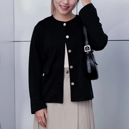 A woman wearing a black cardigan from Vlowy with round neckline and button closures, paired with a beige outfit.