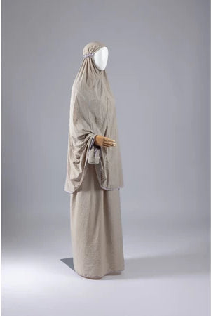Beige mukena from Muhajir Project on a mannequin against a gray background