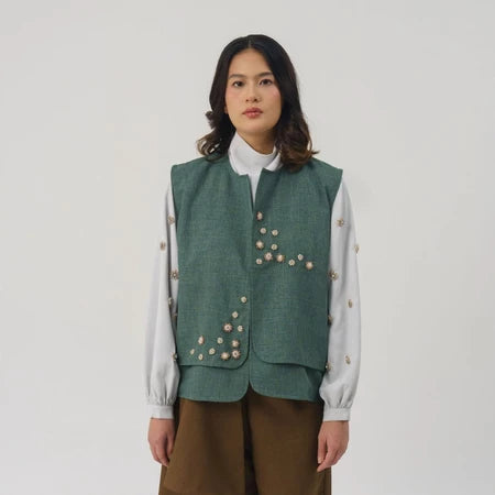 Person wearing a green vest by Jenna & Kaia with floral embroidery on a plain background