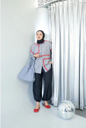 Woman in a grey striped shirt by Abame and hijab standing next to a disco ball with a curtain in the background