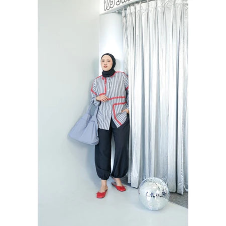 Woman in a grey striped shirt by Abame and hijab standing next to a disco ball with a curtain in the background