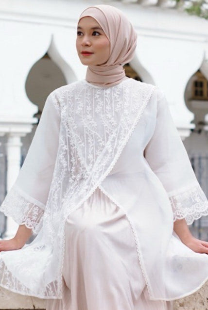 A woman wearing a white shirt with lace details by Casa Elana and a maxi skirt, standing in front of a building with arches.