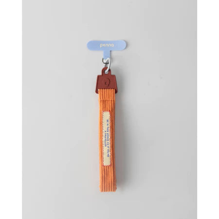 Orange keychain strap with a brown buckle from Muhajir Project on a gray background