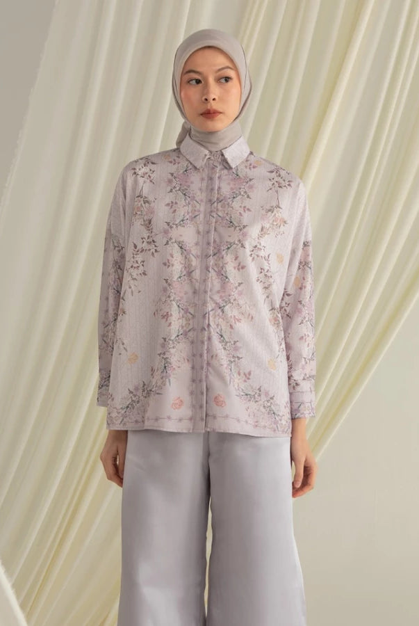 Person wearing a purple floral shirt by Hijabchic and light gray pants against a draped fabric background