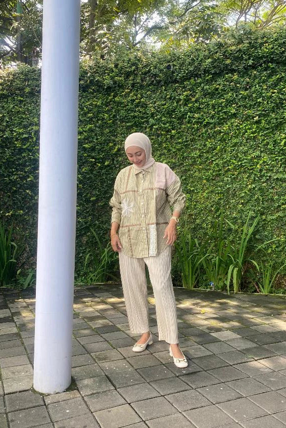 Woman wearing a striped shirt by Abame with olive-colored line accents, holding a coffee cup on a white background
