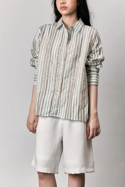 Person wearing a striped shirt by Studio Tui and white shorts against a plain background