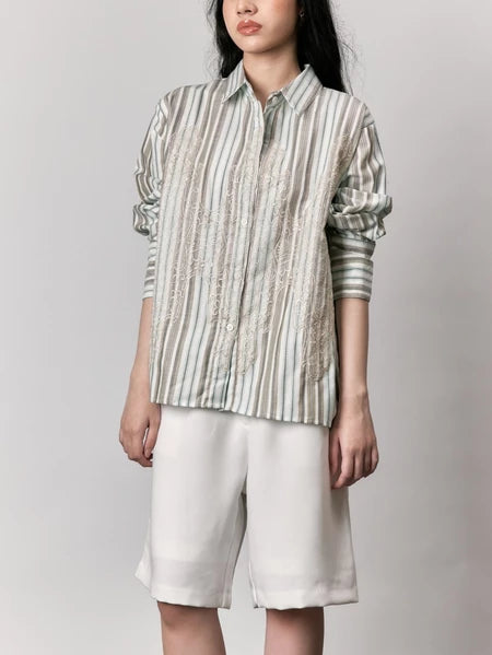 Person wearing a striped shirt by Studio Tui and white shorts against a plain background