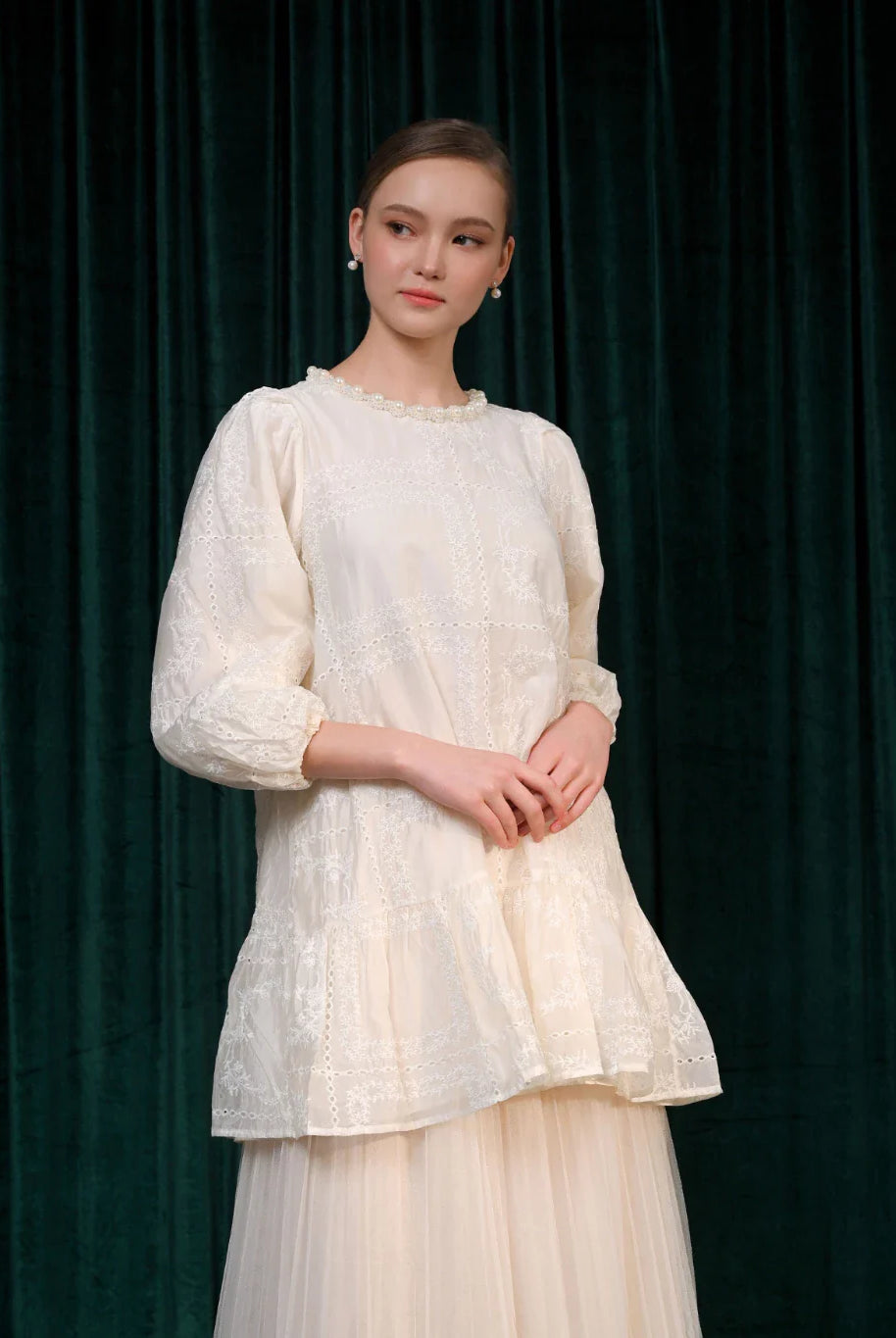 A woman wearing a beige tunic with long sleeves and a round neckline, paired with a pleated skirt.
Seorang wanita memakai tunik berwarna beige berlengan panjang dengan kerah bulat, dipadukan dengan rok pleated.