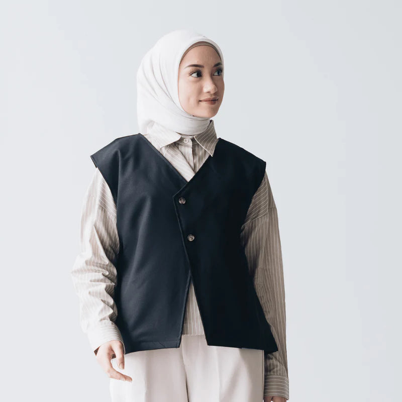 Woman wearing a black vest from Atala Scarves over a light-colored shirt with a white hijab on a plain background