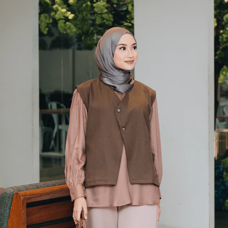 Woman wearing a brown vest from Atala Scarves over a pink shirt with a gray hijab, standing outdoors.
