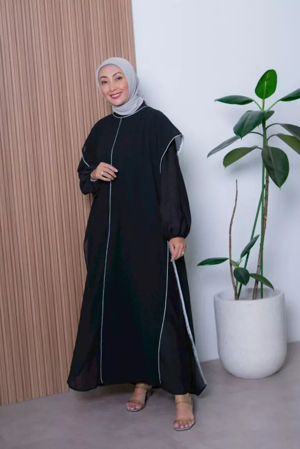 Woman in a black dress by Abame standing next to a plant indoors