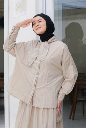 A woman standing outdoors wearing a beige shirt with long sleeves and a round neckline by Casa Elana, the shirt appears to be made of crinkle fabric.