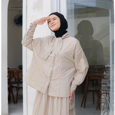 A woman standing outdoors wearing a beige shirt with long sleeves and a round neckline by Casa Elana, the shirt appears to be made of crinkle fabric.