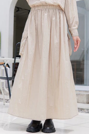 A person wearing a beige maxi skirt with an elastic waistband by Casa Elana, paired with black shoes, standing in a light-colored environment.