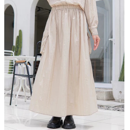 A person wearing a beige maxi skirt with an elastic waistband by Casa Elana, paired with black shoes, standing in a light-colored environment.