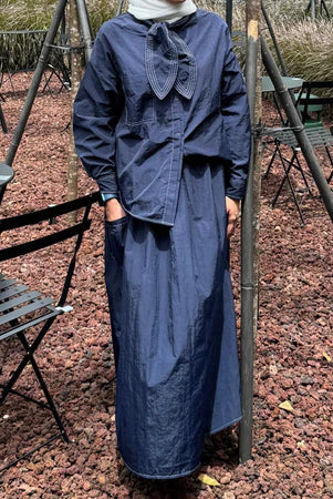 A person wearing a navy maxi skirt with an elastic waistband by Casa Elana, paired with black shoes, standing in a light-colored environment.