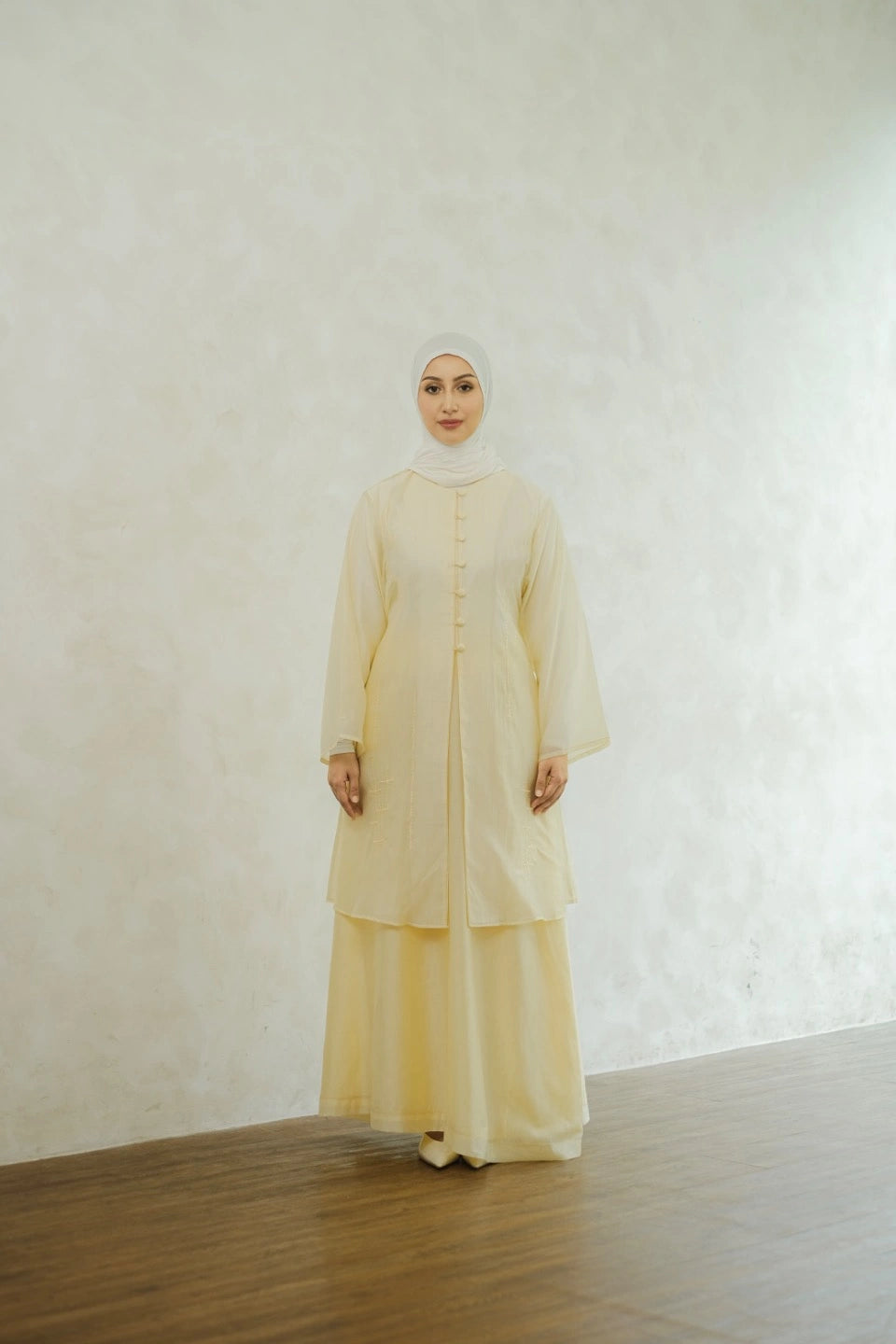 Woman wearing a light yellow tunic by Tufine and hijab against a white wall.
Seorang wanita yang mengenakan tunik berwarna kuning muda dari Tufine dan jilbab, berlatar belakang dinding putih.