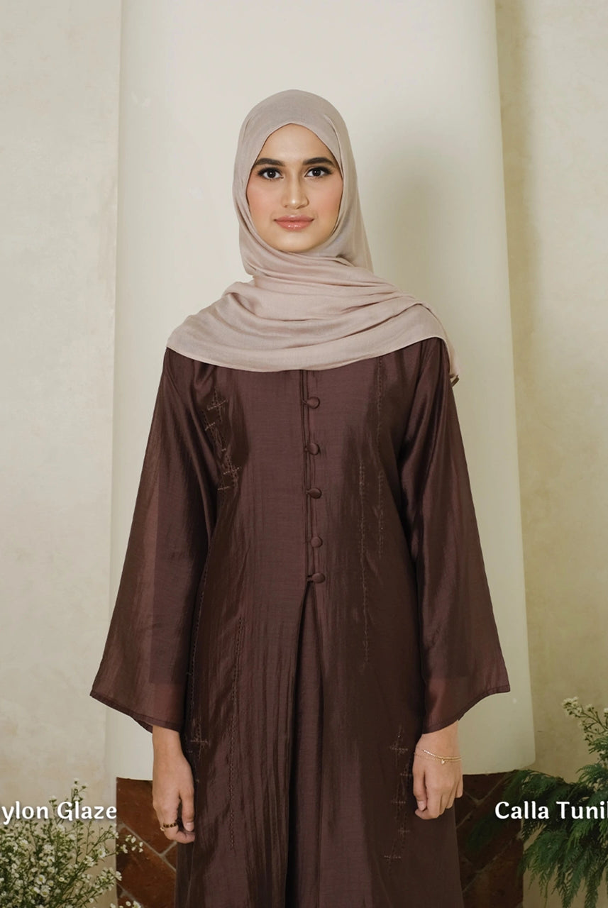 Woman wearing a brown tunic by Tufine with a beige hijab against a white wall.
Seorang wanita mengenakan tunik cokelat dari Tufine dengan jilbab krem di depan dinding putih.