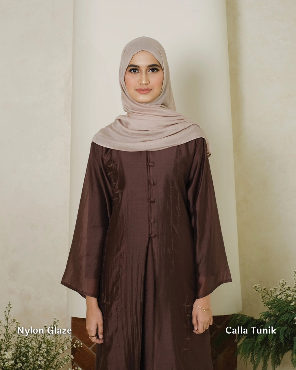 Woman wearing a brown tunic by Tufine with a beige hijab against a white wall.
Seorang wanita mengenakan tunik cokelat dari Tufine dengan jilbab krem di depan dinding putih.