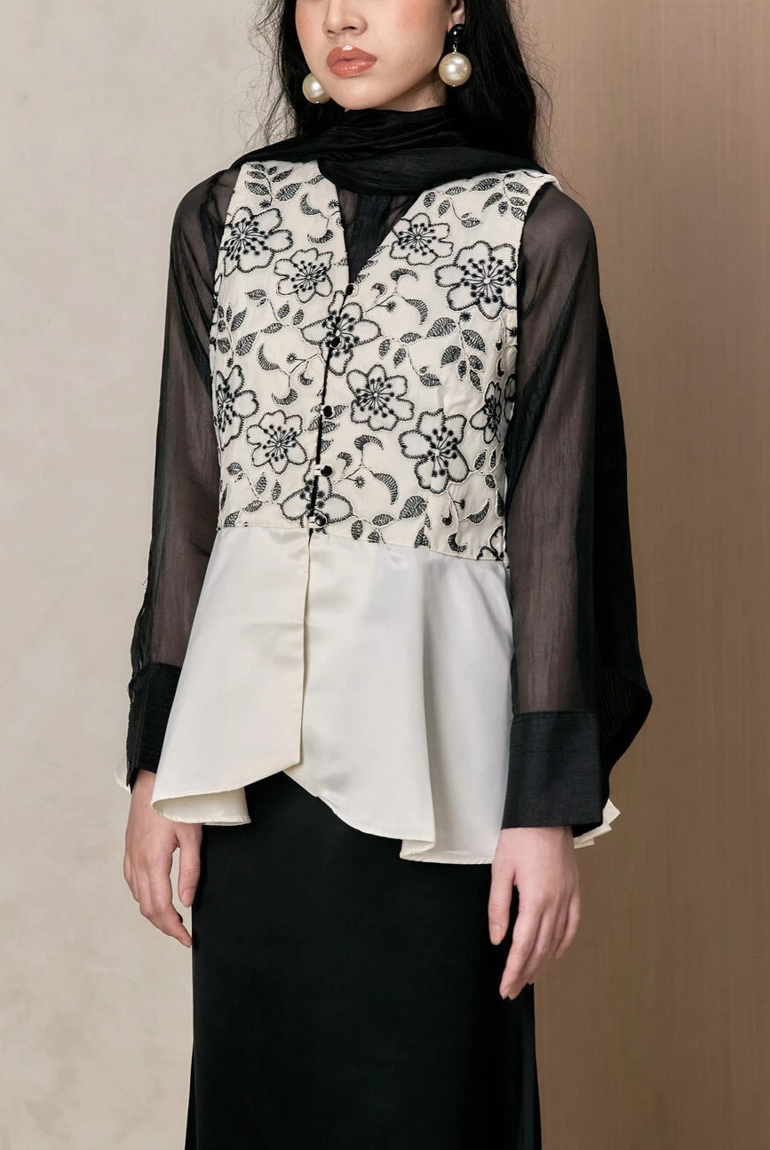Woman wearing a layered outfit with a floral vest and black sheer sleeves by Studio Tui on a beige background